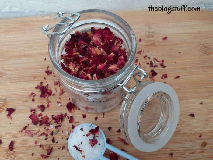 Homemade bath salts with dried rose petals in an open glass jar