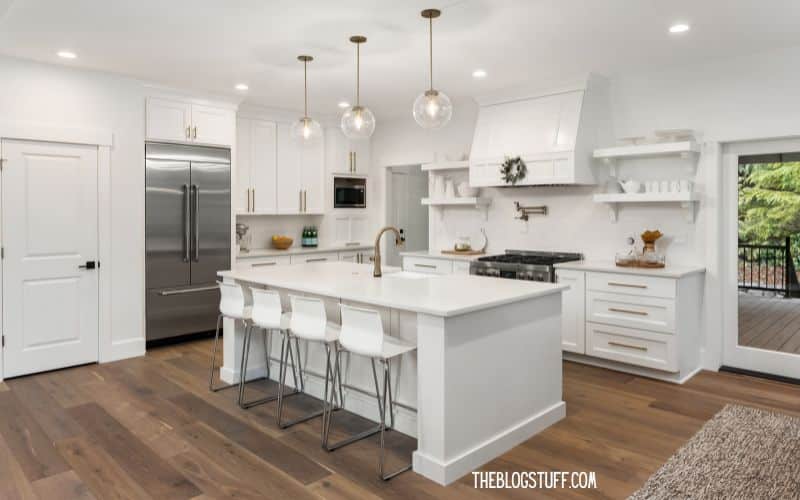 Modern, white kitchen with an island, bar stools, and elegant pendant lights.