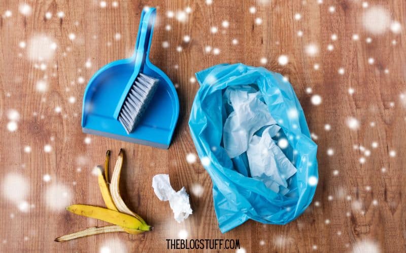 Tips to clean before Christmas: Dustpan, brush, trash bag, and garbage on a wooden floor with a snowy overlay.