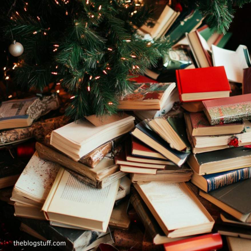 A Christmas tree surrounded by a large pile of books underneath its green branches, creating a cozy and slightly chaotic holiday scene.