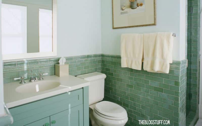 Clean bathroom with green tiles, white countertop, and neatly hung towels.






