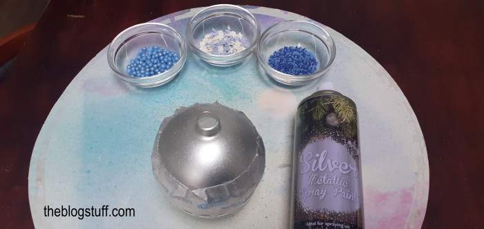 Cake sprinkles, faux snow, a bauble, and silver spray paint