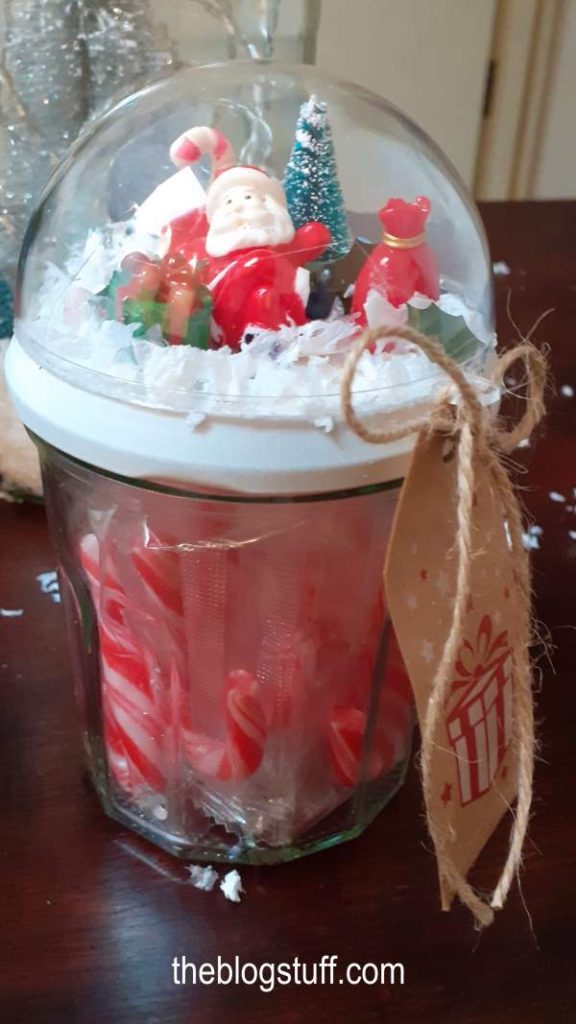 A Mason jar filled with candy and decorated with Christmas ornaments