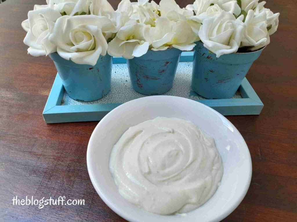 Homemade hair mask in a bowl with flowers on a blue tray as background