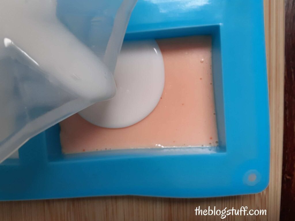 Pouring white soap over orange soap in a silicon mold