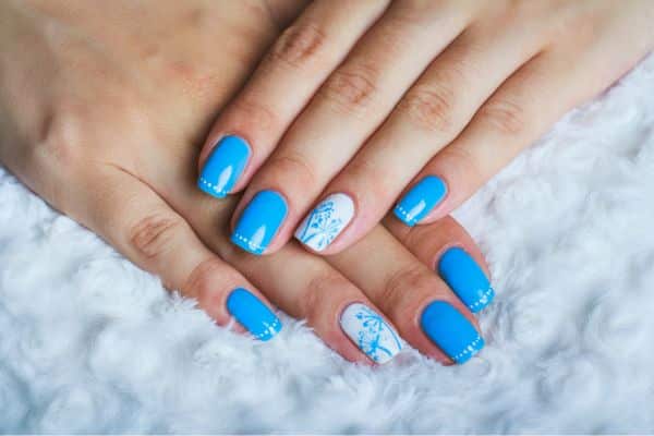 Sky blue nails with a floral pattern in white and blue in some of the nails