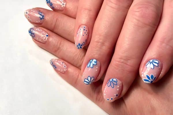 Alomond shaped nails with a clear base dressed with blue flowers and tiny blue dots