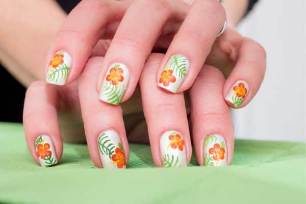 Square nails on a white base decorated with spring orange flowers and green leaves