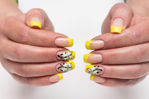 Frenc manicure with tellow tips and a butterfly design in 3 of the nails