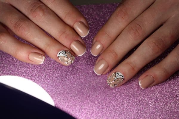 Short nude nails with an embellished butterfly design in two of the nails