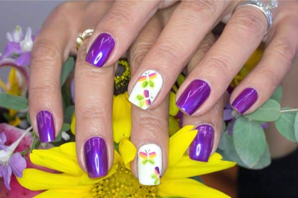 Purple manicure with two of the nails in white with a butterfly design