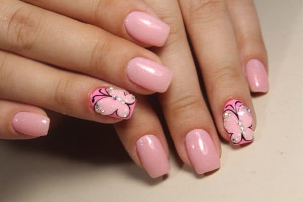 Soft pink nails with a sparkle butterfly design in two of the nails