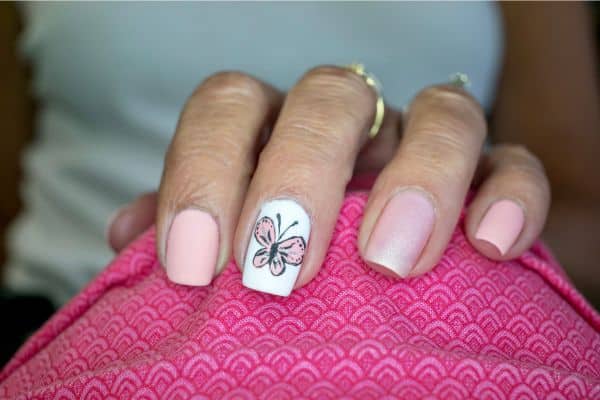 Light pink nails with a butterfly design in one nail