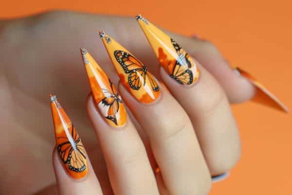 Orange stiletto nails with a black butterfly design