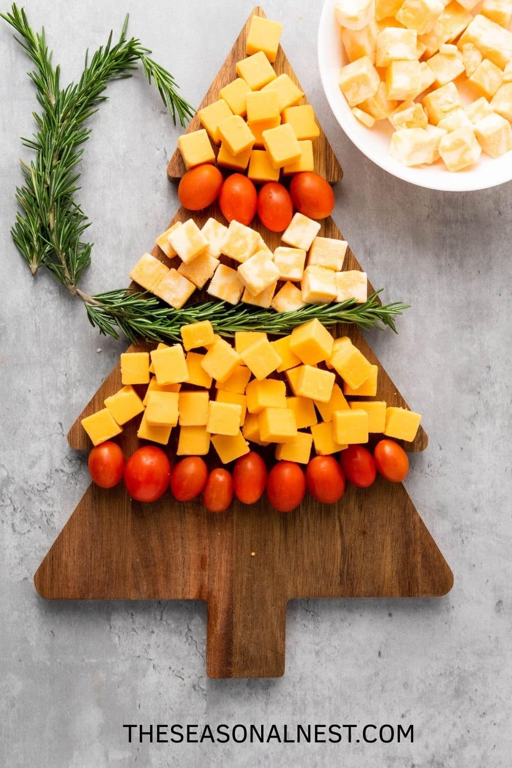Making a Christmas Tree Cheese with rosemary springs over a Christmas tree board.