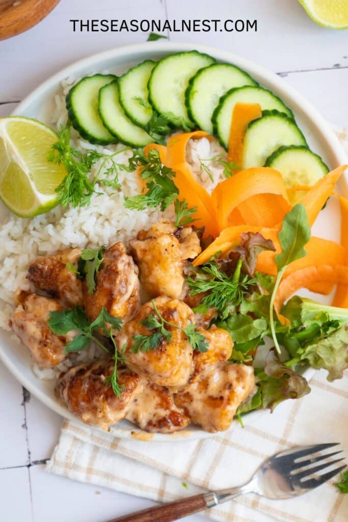 Bang Bang Chicken rice bowl with crispy chicken, white rice, cucumber slices, carrot ribbons, fresh greens, and lime wedges.