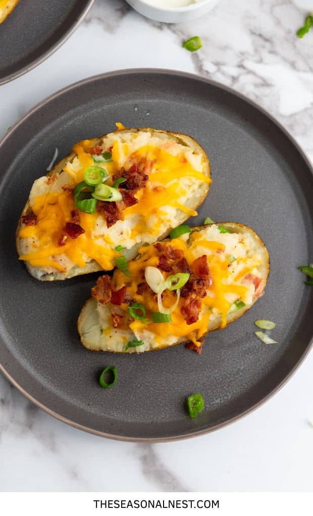 Cheesy stuffed baked potatoes topped with crispy bacon and sliced green onions on a dark plate.
