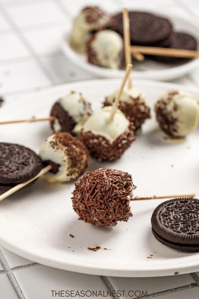 Dipped Oreo cake pops with chocolate sprinkles and Oreo cookies on a plate.