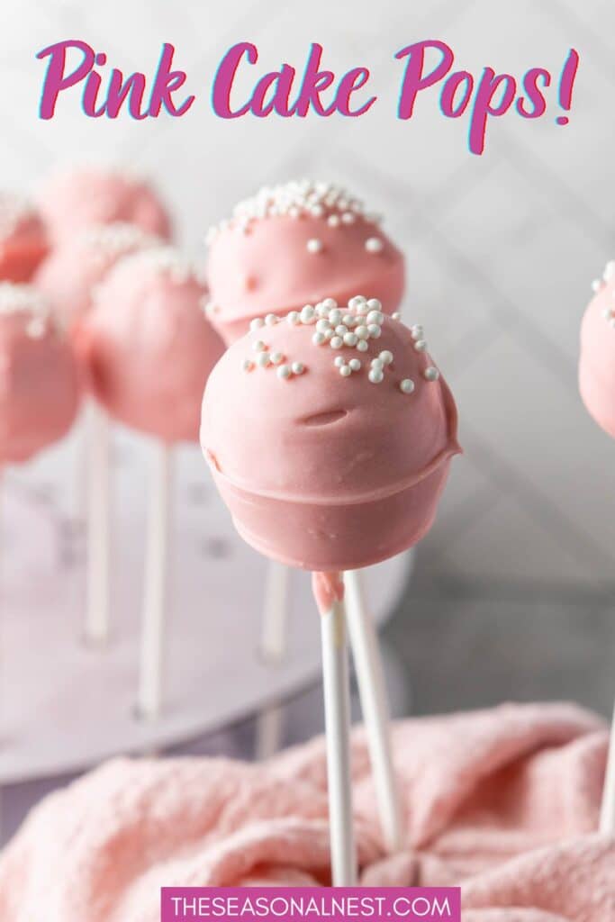 Close up of pink cake pops with white sprinkles displayed on a cake pop stand with a soft pink cloth.