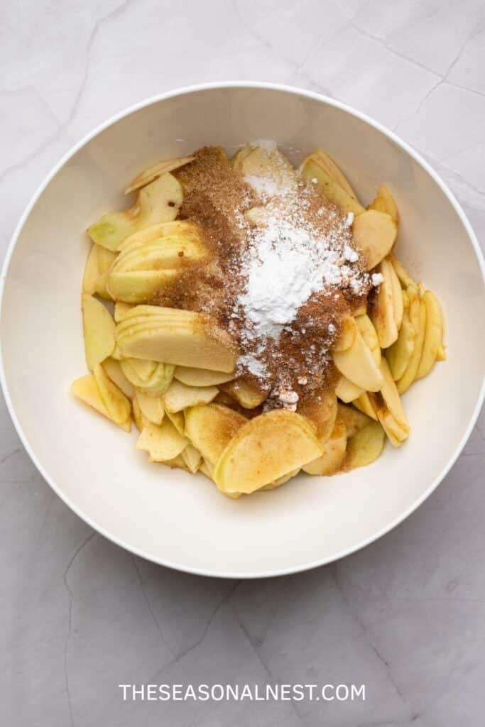 Bowl of sliced apples mixed with sugar, cinnamon, and cornstarch ready for baking.