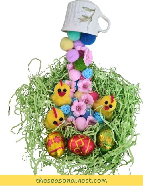 Cute floating tea cup craft with a cascading Easter-themed display of pom-poms, artificial flowers, and mini chicks, surrounded by shredded paper and colorful eggs.