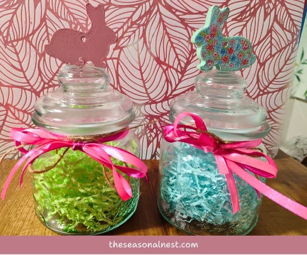Easter mason jars filled with pastel shredded paper, tied with twine and pink ribbon, with bunny decorations on the lids