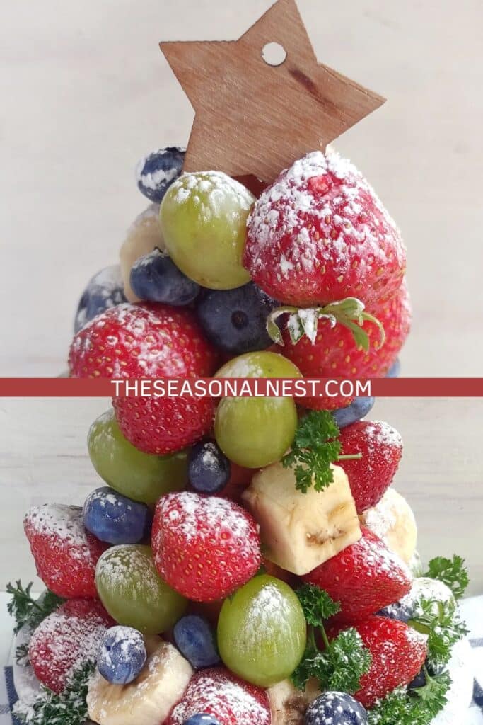 Close-up of a fruit Christmas tree topped with a wooden star and dusted with powdered sugar.