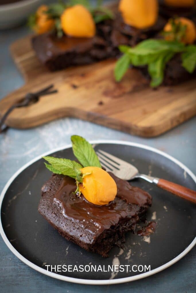 Single Halloween brownie topped with chocolate ganache, a strawberry pumpkin, and fresh mint on a black plate.