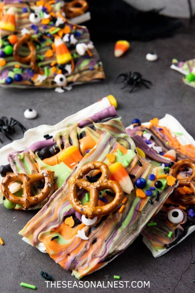 Broken Halloween bark with pretzels, candy corn, sprinkles, and edible candy eyes on a dark background.