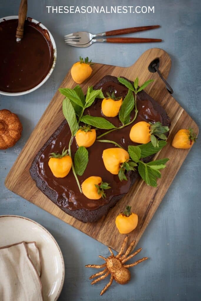 Halloween brownie cake topped with chocolate ganache, orange-dipped strawberries styled as pumpkins, and fresh mint leaves for a festive fall dessert.