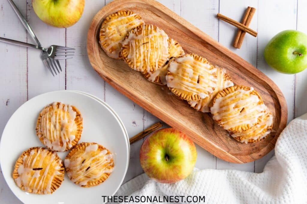 Mini hand pies on a wooden tray with real apples, forks and white plates.