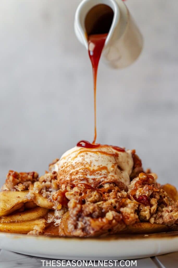 Close-up of apple crisp topped with vanilla ice cream and drizzled with caramel sauce.