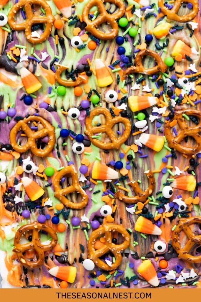 Festive Halloween candy bark topped with pretzels, candy corn, sprinkles, and edible eyes on a dark background.