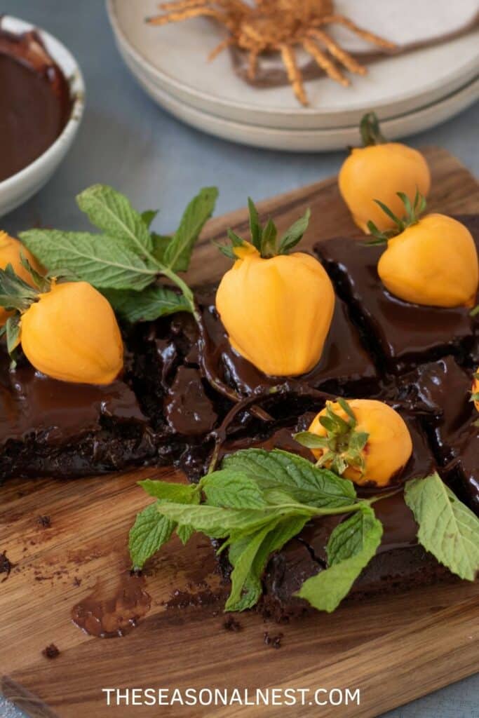 Halloween brownies topped with chocolate ganache, strawberry pumpkins, and fresh mint leaves for a festive pumpkin patch dessert.