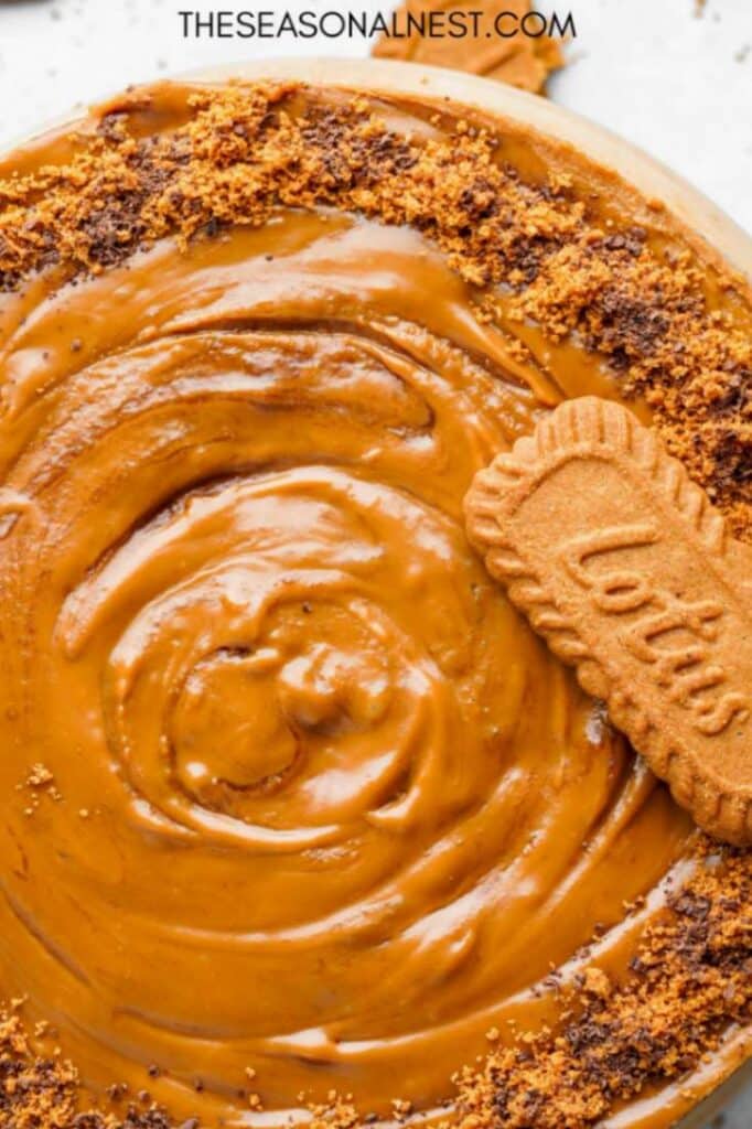 Close-up of creamy Biscoff cheesecake topped with glossy cookie butter and crushed Lotus biscuits.