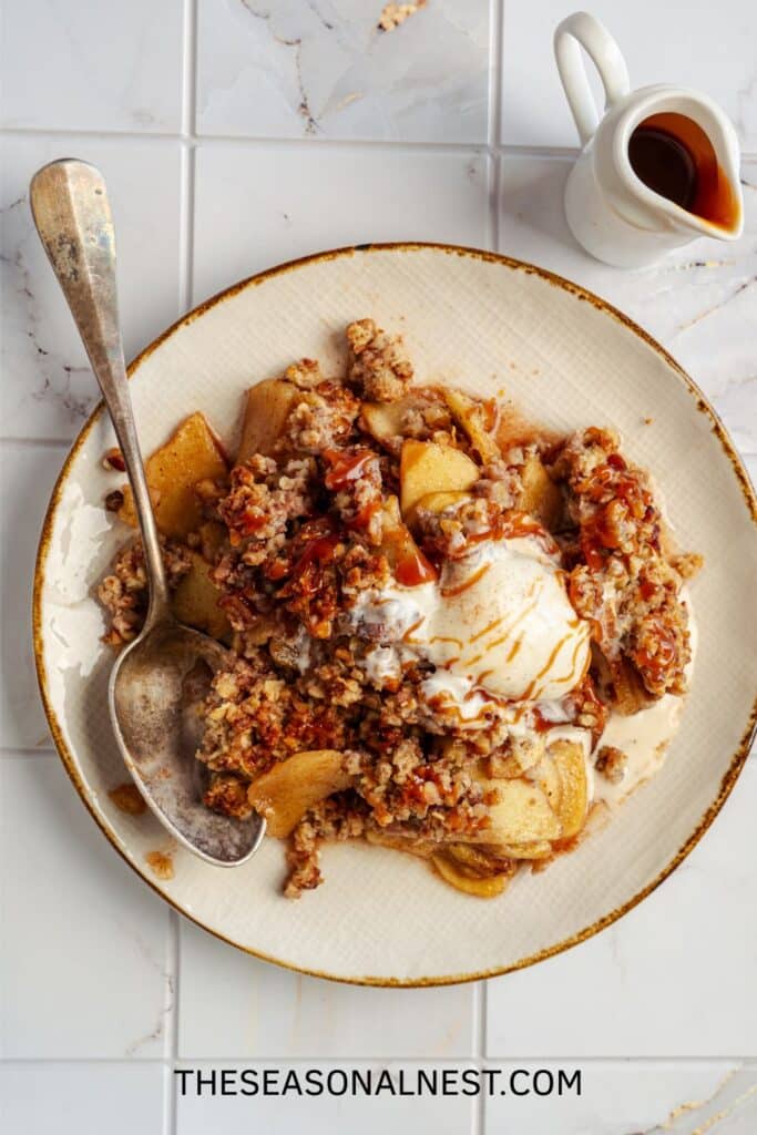 Plate of apple crisp with vanilla ice cream and caramel sauce, served with a spoon.