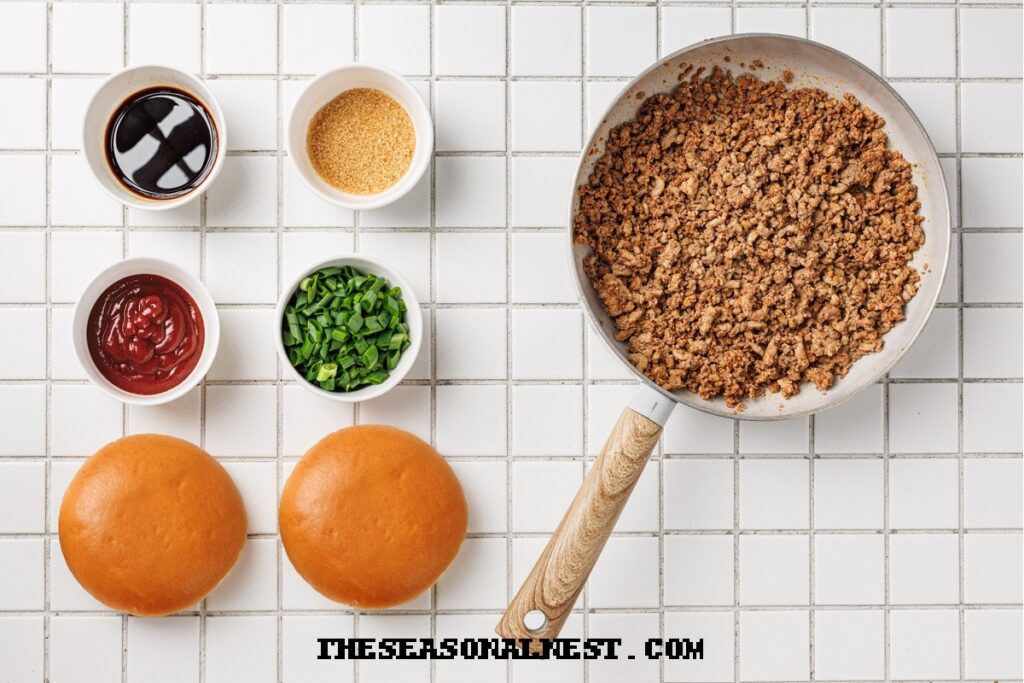 Skillet of seasoned beef with ketchup and sugar added, next to fresh buns and scallions