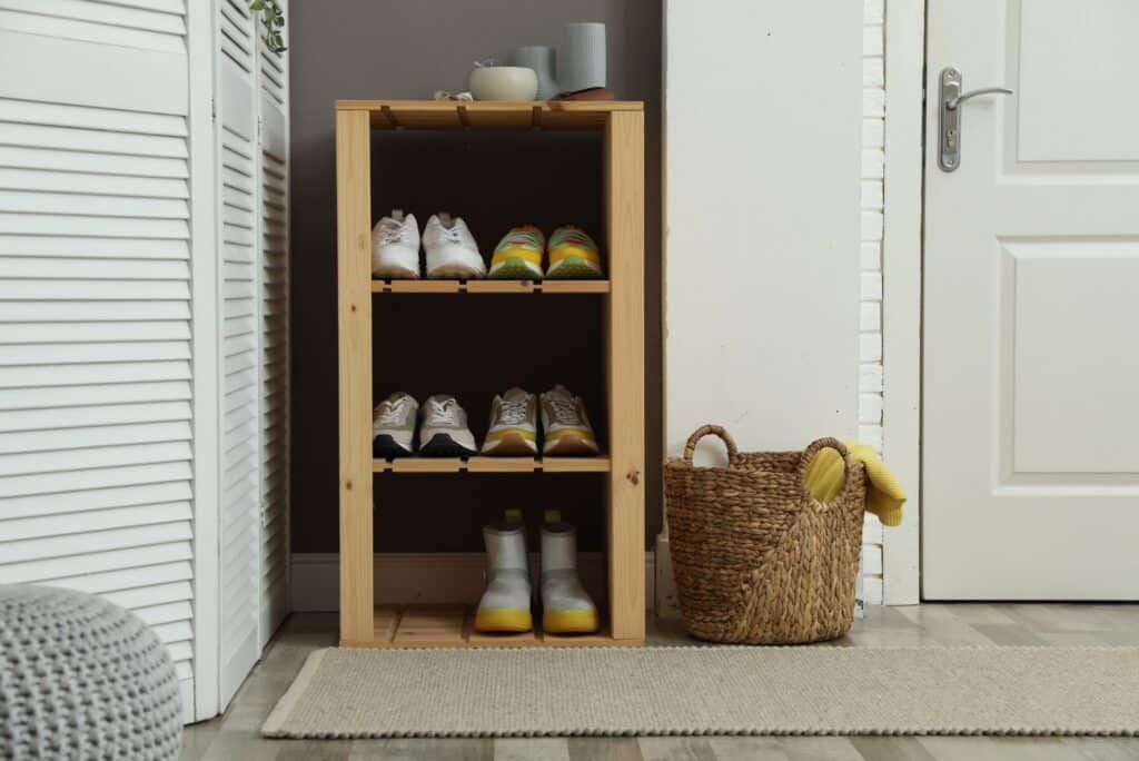 Organized entryway with wooden shoe rack, neatly arranged shoes, woven basket, and clean floor mat.