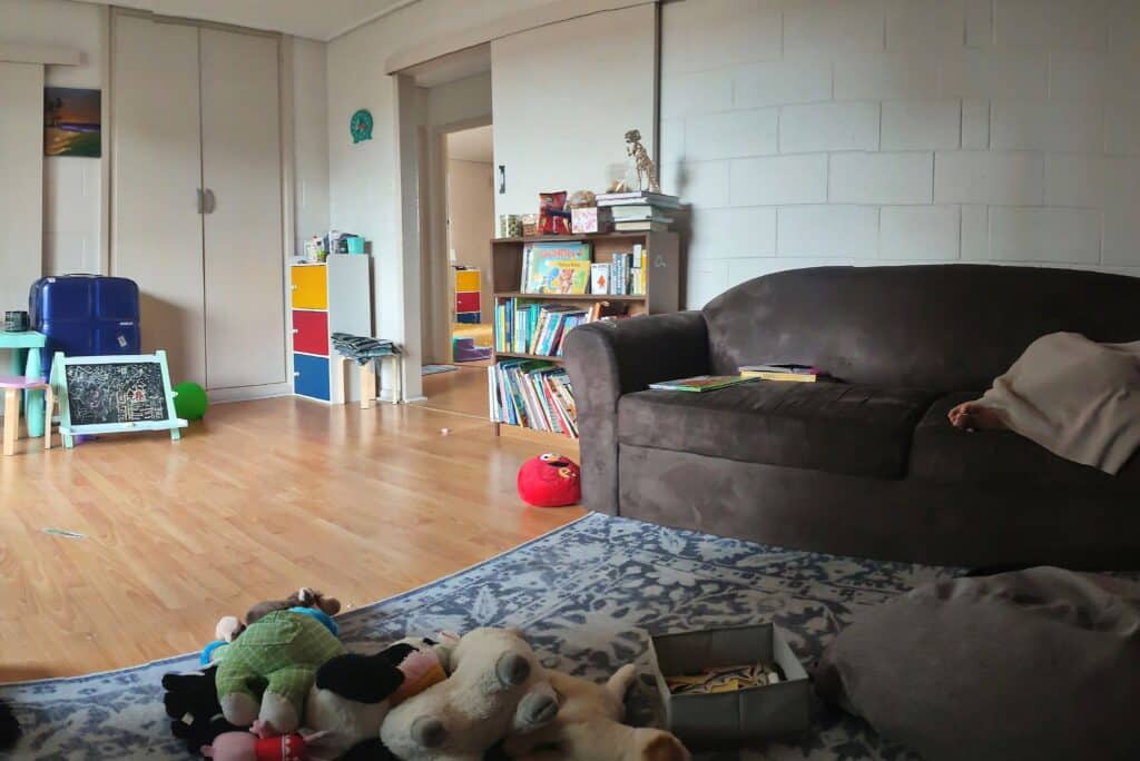 Living room with toys scattered on the floor and sofa, showing a messy space ready for decluttering and cleaning.
