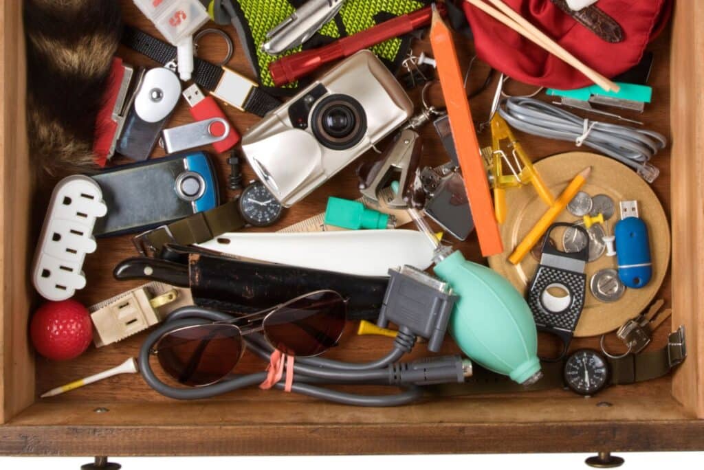 Overfilled junk drawer packed with random household items, cables, tools, and small electronics ready for decluttering.