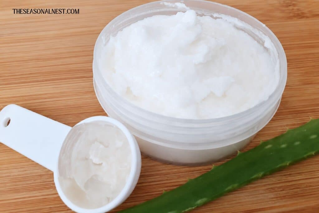 Homemade aloe vera face cream  with a spoon full of aloe vera gel and an aloe vera leaf.