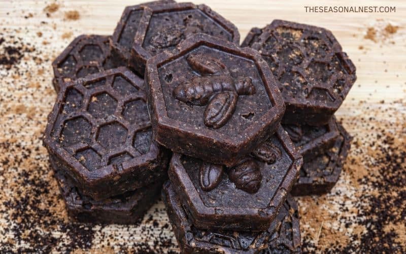 Top view of sugar and coffee scrub cubes with scattered cinnamon powder and coffee grounds over a wooden surface.