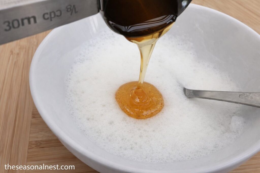 Pouring honey on whisked egg white to make a DIY skin tightening face mask.