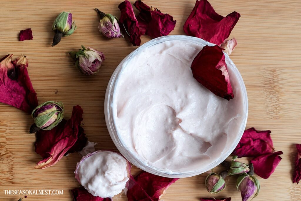 Rose water face cream in a container surrounded by rose petals.