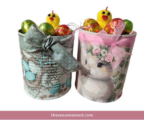 Two tin cans decorated for easter with napkin designs, filled with chick figurines, and chocolate eggs.