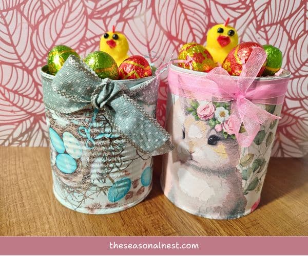 Two decorated Easter tin cans with pastel napkin designs, filled with chocolates and small chick figurines.