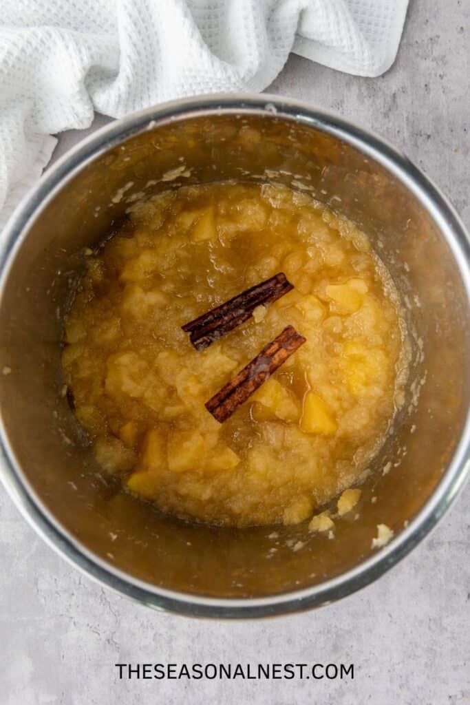 Cooked apples with cinnamon sticks inside an Instant Pot, ready to be mashed into applesauce.
