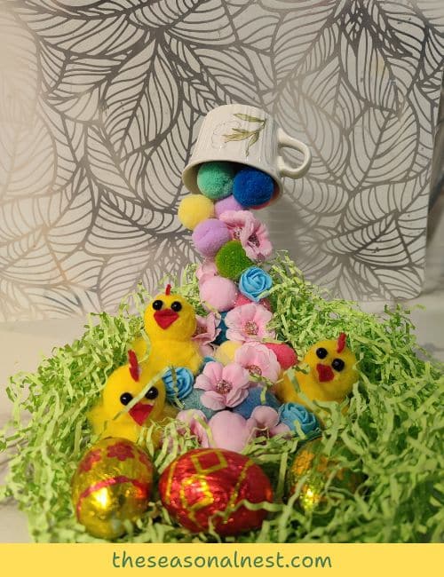 A floating tea cup Easter decoration featuring cascading pom-poms, artificial flowers, and chocolate eggs, creating a festive and whimsical centrepiece.