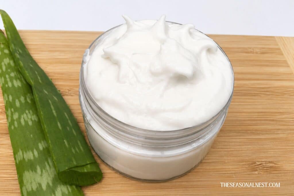 DIY aloe vera face cream in a container with an aloe vera leaf besides.