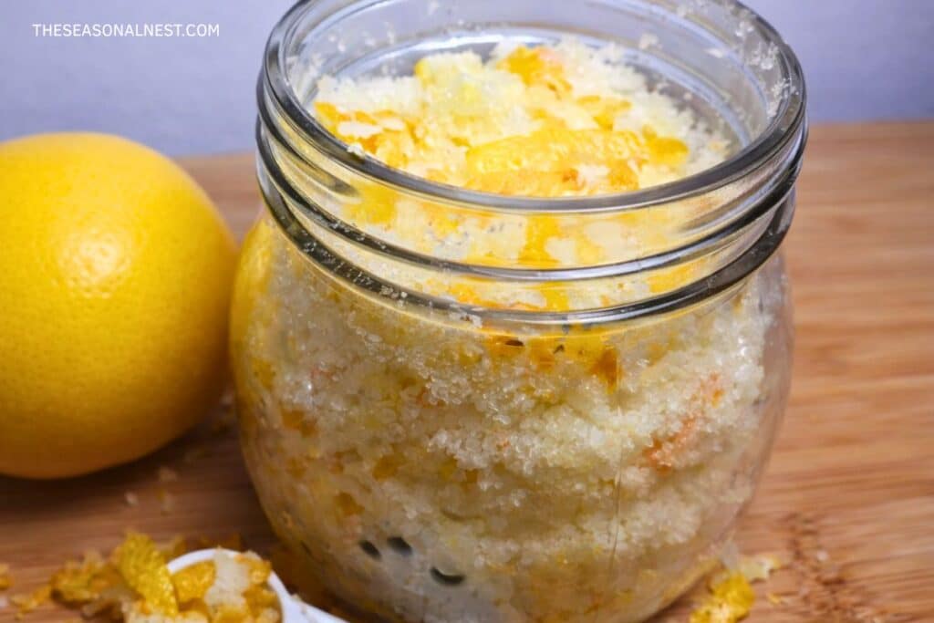 DIY lemon scrub with lemon peel in a jar and a fresh lemon bsides the jar. A spoon with lemon peels.